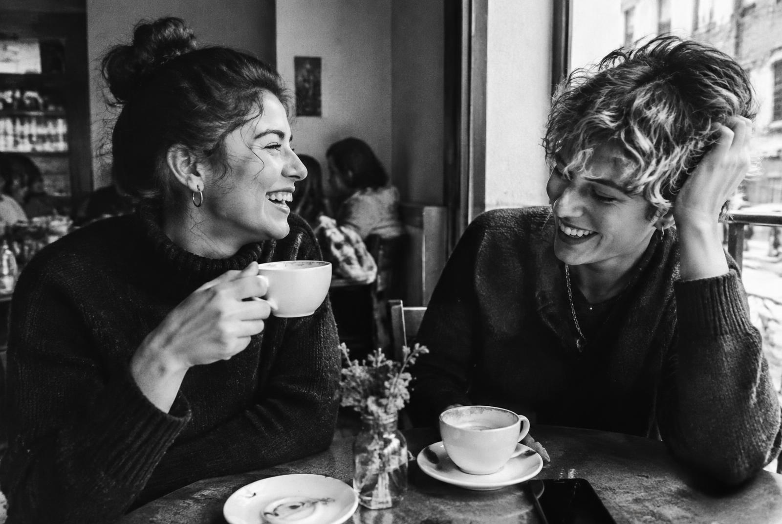 Two queer women laughing together over coffee